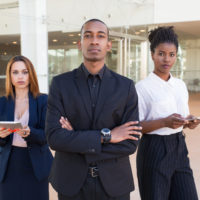 Successful business team posing in office hall. Three mix raced professionals with arms crossed standing in office hall and looking at camera. Multiethnic business team concept